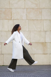 Young woman walking on footpath by wall