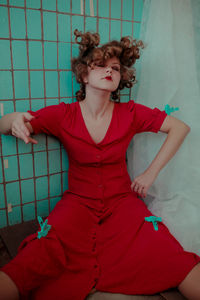 Young woman in red dress with closed eyes gesturing against wall