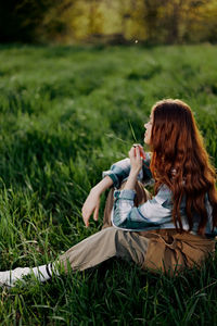 Side view of woman sitting on grassy field