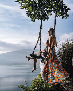 Woman swinging over sea against sky