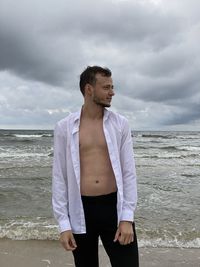 Young man standing at beach against sky