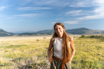 Young woman standing on field against sky