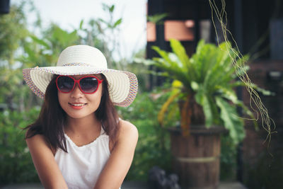 Portrait of beautiful young woman wearing sunglasses and hat while sitting at yard