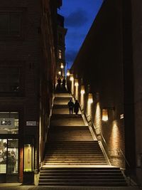 Person walking on illuminated steps amidst buildings in city
