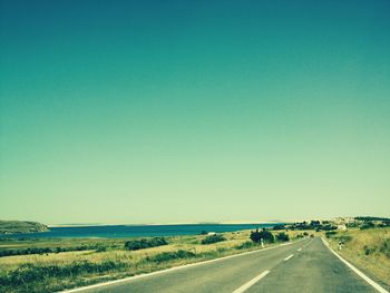 Road passing through land against clear blue sky