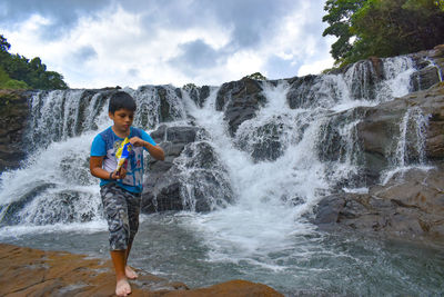 Portrait of young woman standing against waterfall