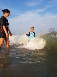 Mother and son enjoying in sea against sky