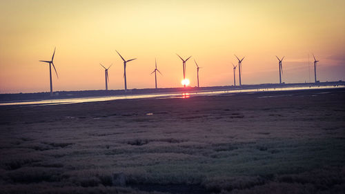 Wind turbines on field against sky during sunset