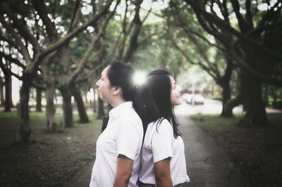 Friends standing back to back against trees at park