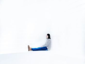 Side view of woman sitting against white background