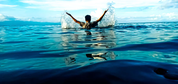 Rear view of teenage boy with arms raised swimming in sea