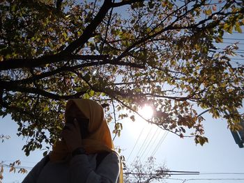 Low angle view of woman sitting on plant against sky