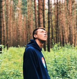 Young man looking up while standing in forest