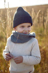 Boy in warm clothes stand on chair along a path on a field with dried grass in autumn