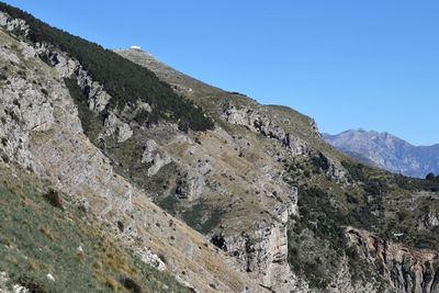 Low angle view of rocky mountains against clear blue sky