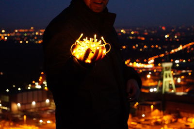 Midsection of man with illuminated cityscape against sky at night