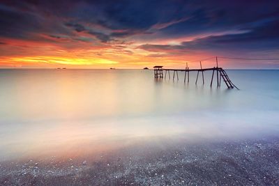 Silhouette pier in sea against cloudy sky during sunrise