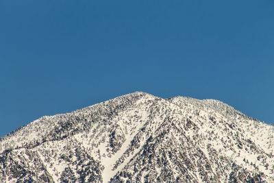 Low angle view of snowcapped mountains against clear blue sky