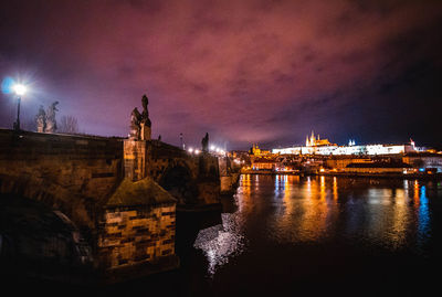 Illuminated buildings by river against sky at night