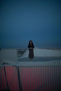 Full length of woman standing by railing against clear blue sky at dusk