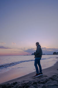 Full length of man standing on beach against sky during sunset