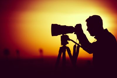 Side view of silhouette man photographing from camera during sunset