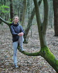 Full length of woman standing by tree trunk in forest