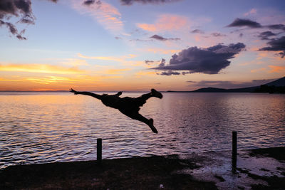 Silhouette man jumping at beach against sky during sunset