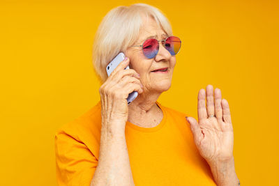 Senior woman talking on phone against yellow background