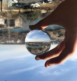 Close-up of hand holding crystal ball against sky