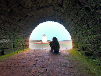 Side view of woman sitting on footpath in tunnel