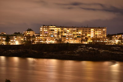 Illuminated buildings by sea against sky at night