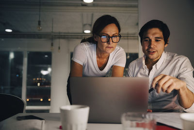 Confident businesswoman planning strategy with businessman during late night meeting at office