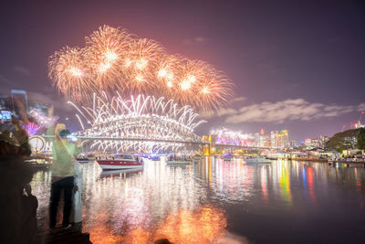 Firework display over river against sky at night