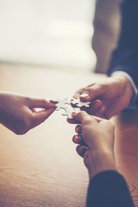 Cropped hands of friends joining jigsaw pieces over table