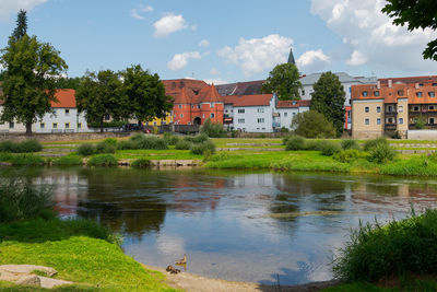 Houses by lake and buildings against sky