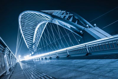 Illuminated bridge against blue sky at night