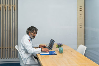 Side view of senior male medic having video call with patient during telemedicine consultation in hospital