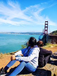 Woman and daughter sitting with golden gate bridge over bay over water in background