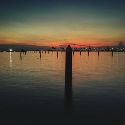 Silhouette wooden posts in lake against sky during sunset
