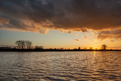 Dark cloud over the lake, trees on the horizon and beauty sunset