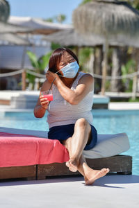 Young woman using phone while sitting in swimming pool