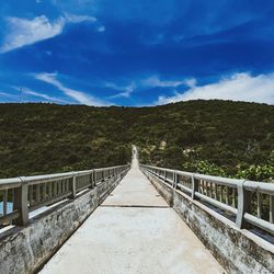 Footbridge leading towards mountains against sky