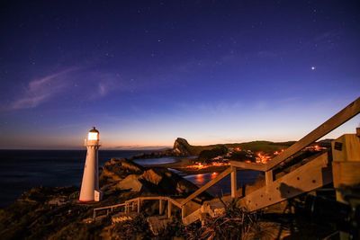 Lighthouse by sea against clear blue sky at night