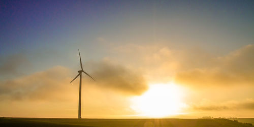 Windmill on field against cloudy sky during sunset