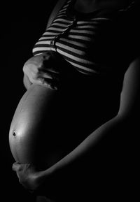 Midsection of woman holding pregnant abdomen against black background