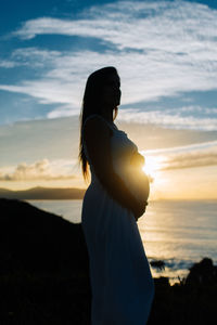 Side view of silhouette woman standing on beach during sunset