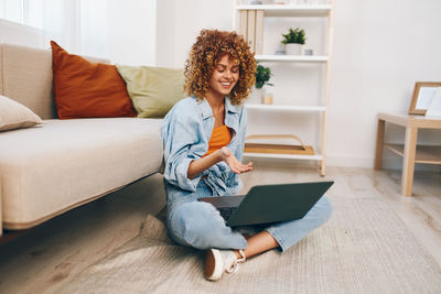 Young woman using laptop while sitting on sofa at home