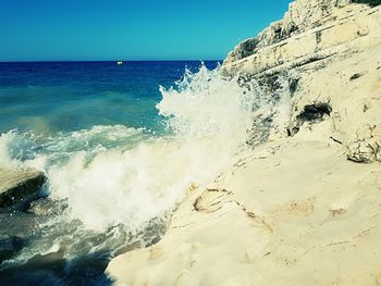 Close-up of waves splashing on beach against clear sky