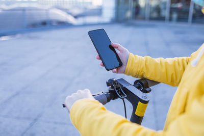 Young woman in yellow coat prepares and uses her electric skateboard.